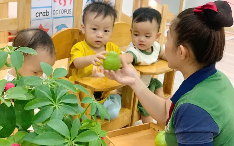 Bé cầm lá cây khám phá trong giờ học ngoài trời